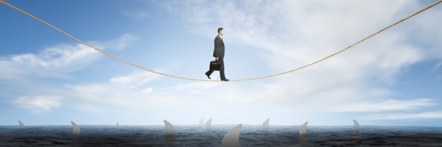 A businessman holding a briefcase walking a tightrope above shark-infested waters